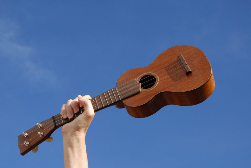 Woman holding a soprano ukulele up in the air against clear blue sky with copy space