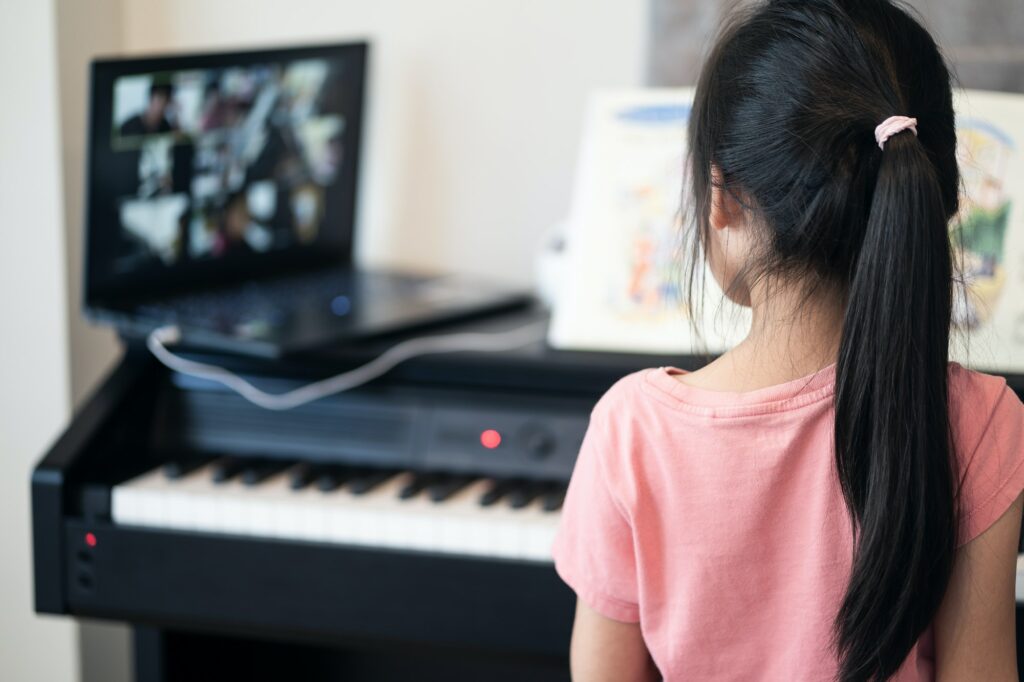 Asian little girl learning piano from computer connecting to internet music online class by school.